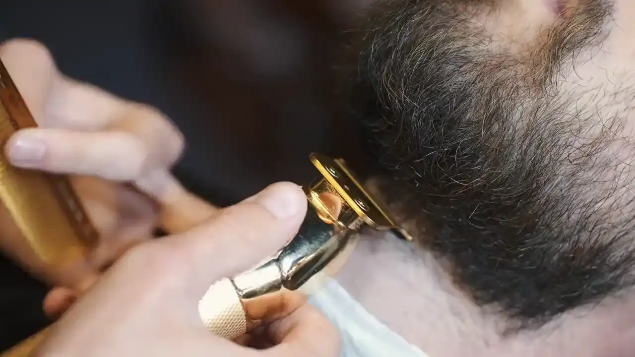 Nahaufnahme: ein Bart wird mit Kamm und goldenem Trimmer in Form gebracht