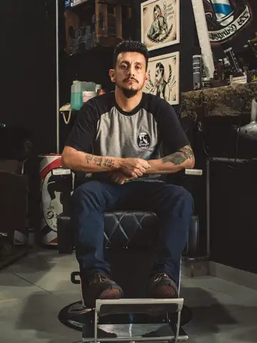 Ein Barbier mit tätowierten Armen sitzt in einem Barbierstuhl