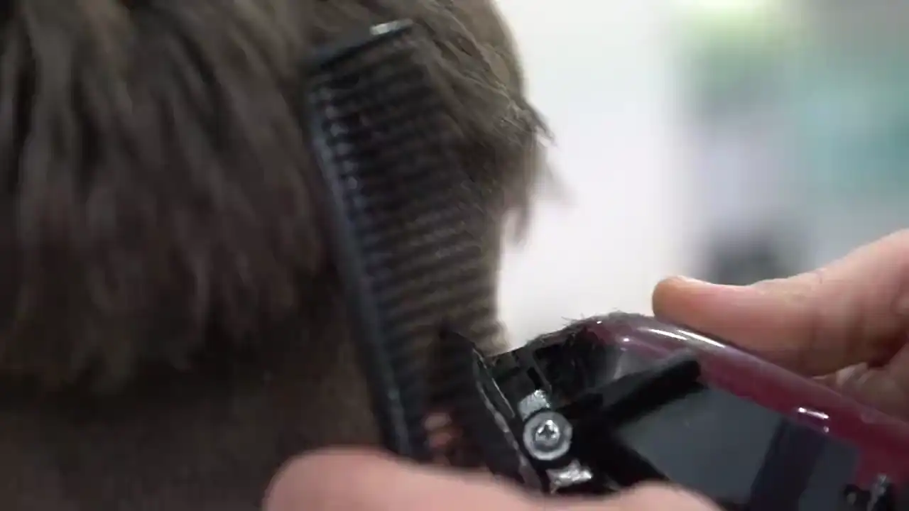 Nahaufnahme: ein Barbier schneidet mit Kamm und Haarschneider einen Übergang in den Nacken