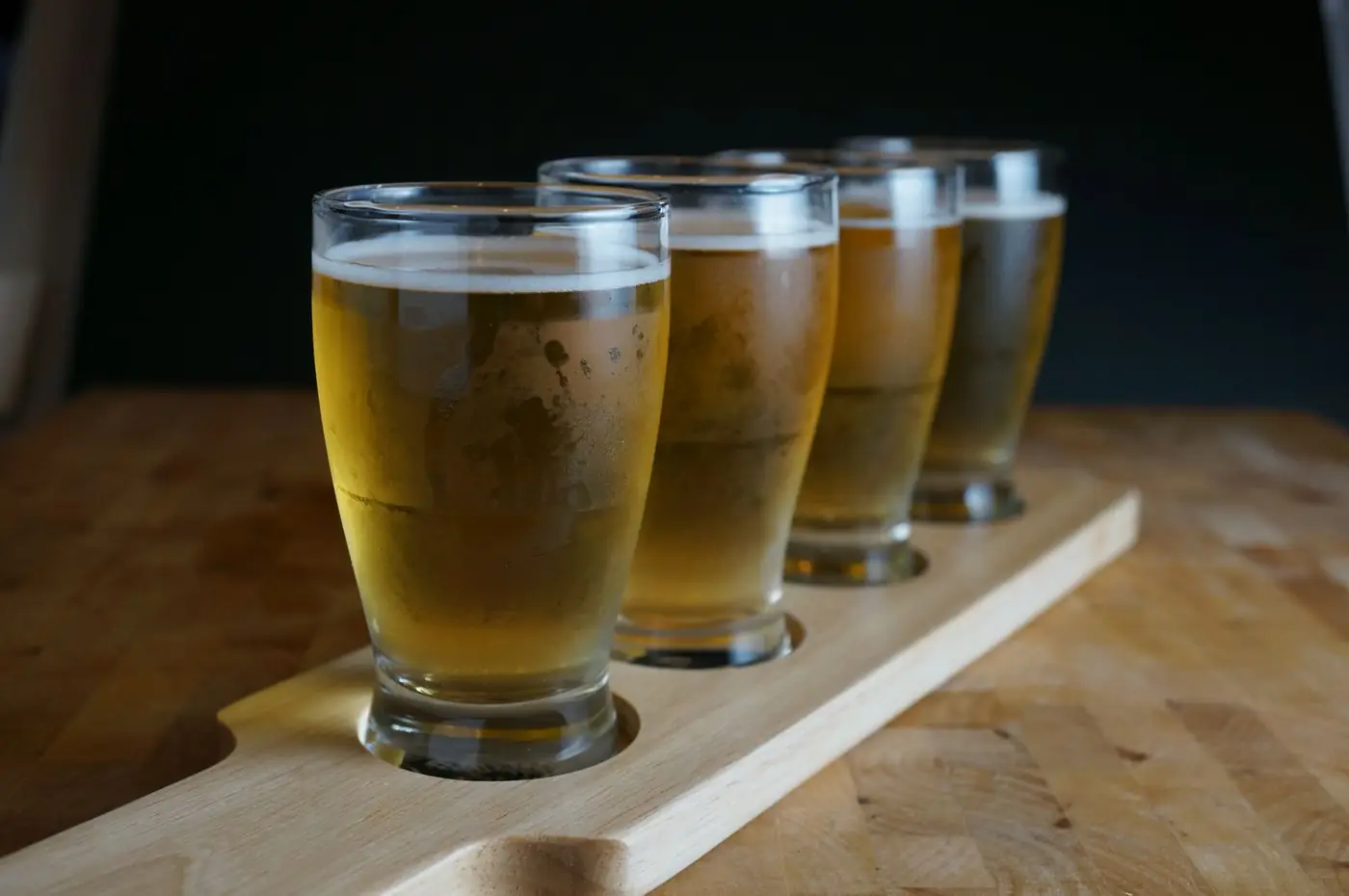 Vier kleine Biergläser in einer Holzleiste, von hell bis bernsteinfarben