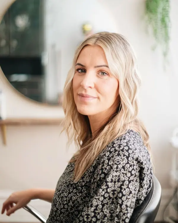 Friseurin mit langen blonden Wellen, sitzend im Salon