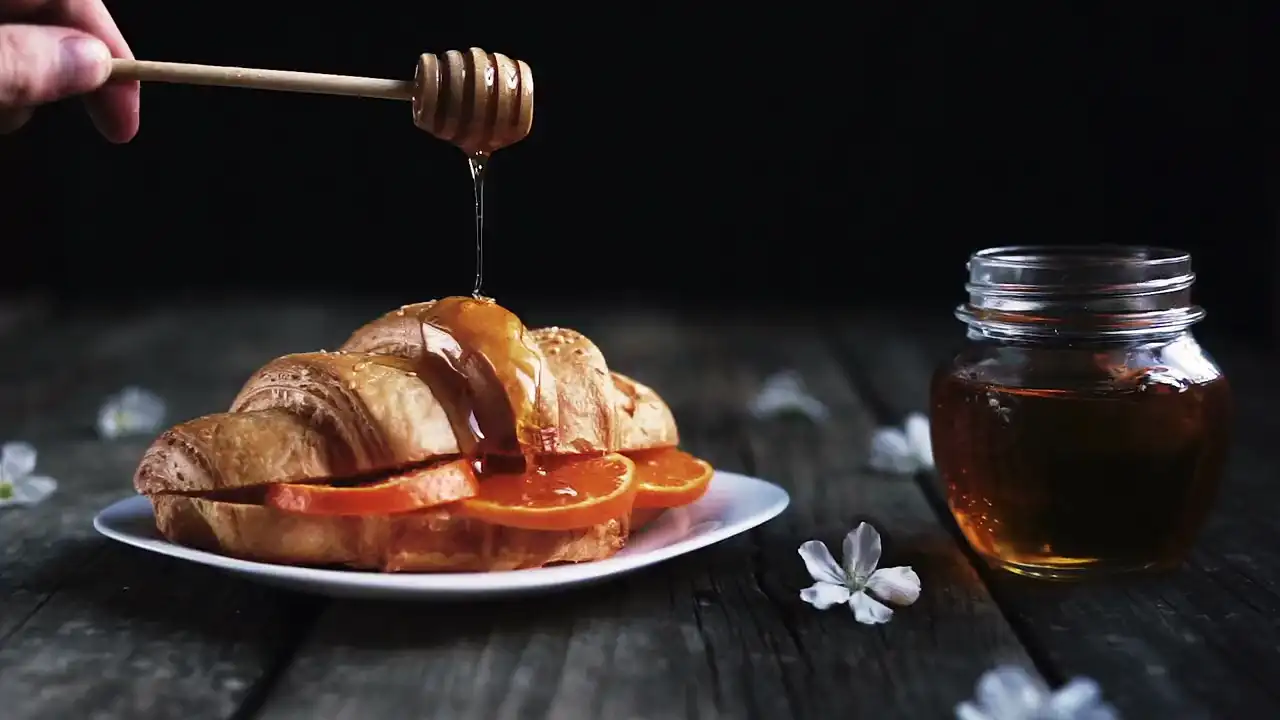 Honig läuft von einem Holzlöffel auf ein Croissant