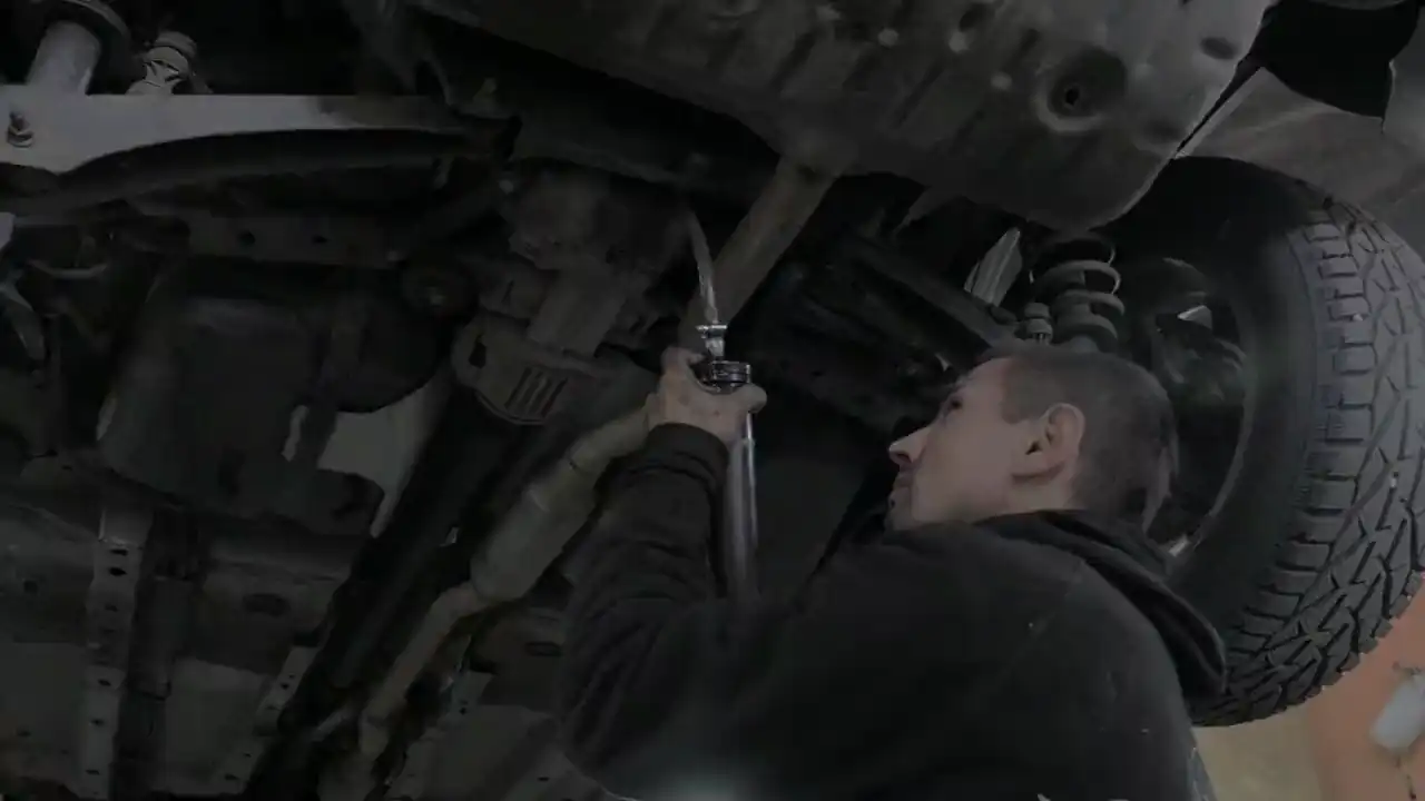Ein Mechaniker sieht sich mit einer Lampe die Unterseite eines Autos an