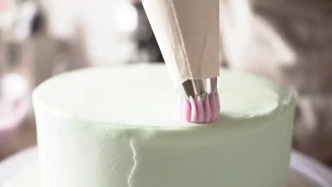 Eine rosa Sahnerosette wird mit dem Spritzbeutel auf eine Torte gesetzt