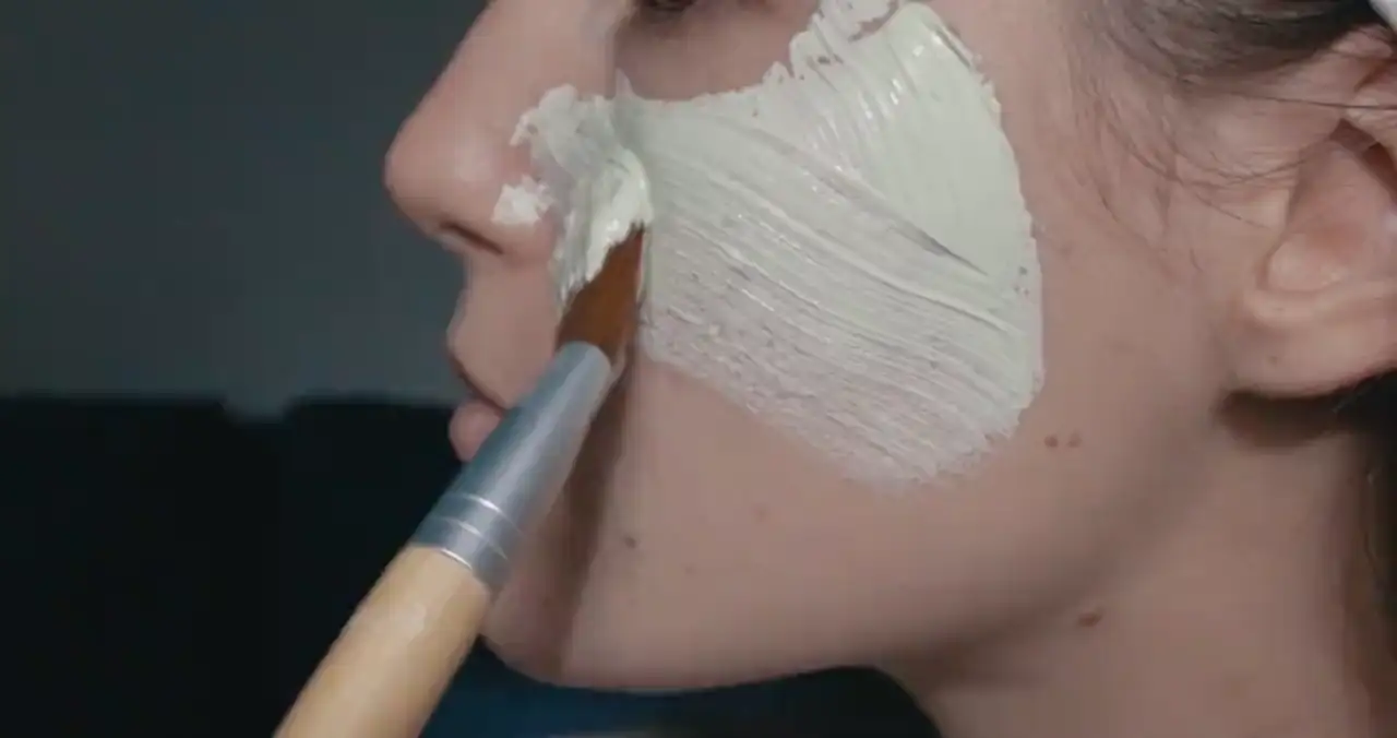 Ein Pinsel verteilt eine helle Maske auf einer Wange