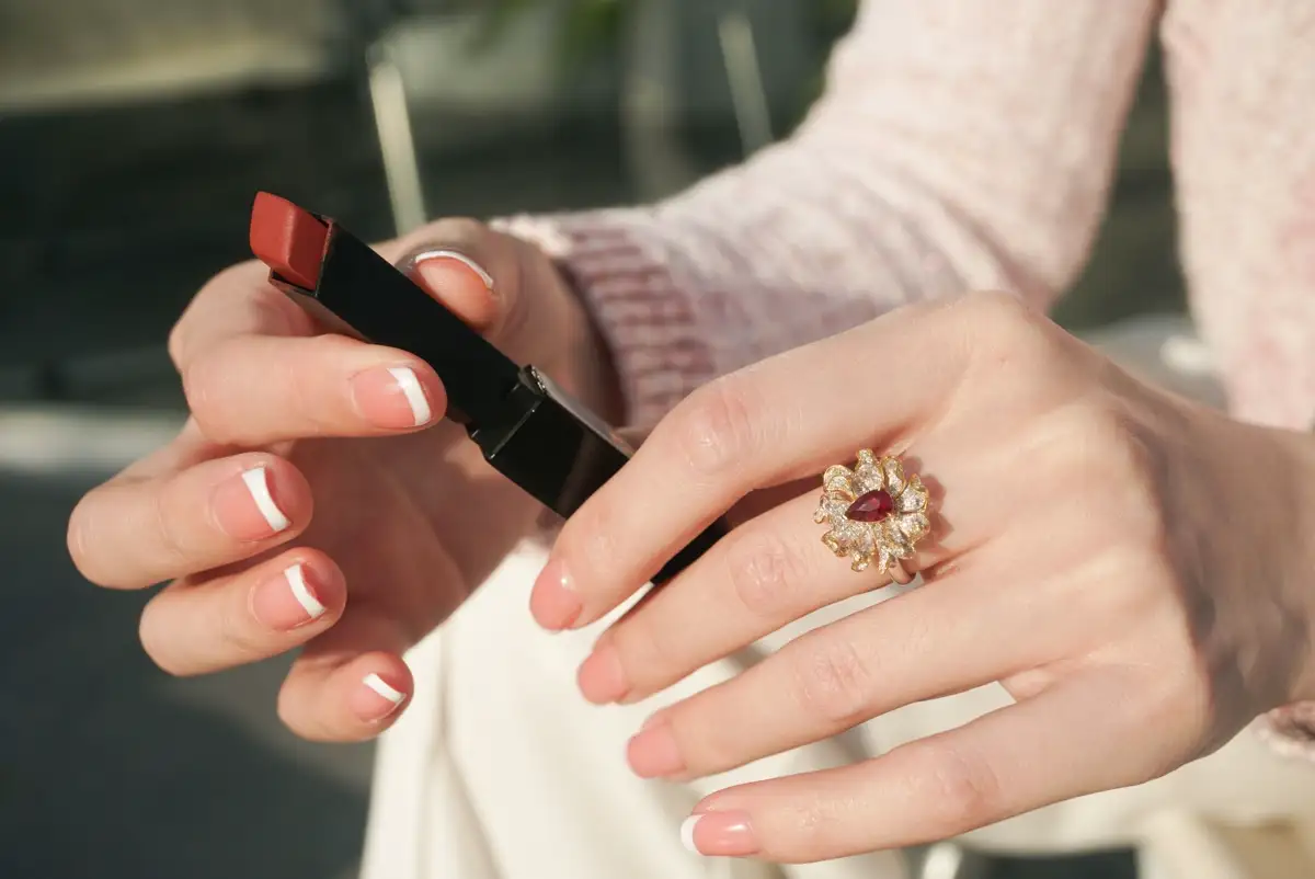 Hände mit French-Maniküre, weiße Spitzen, ein Lippenstift in der Hand