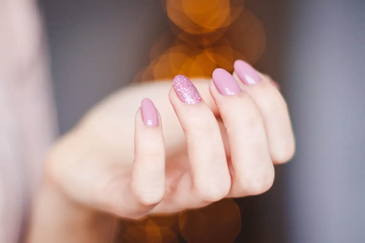 Eine Hand mit rosa Gelnägeln, ein Nagel glitzert