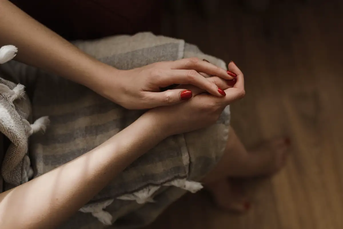Zwei Hände mit kirschrot lackierten Nägeln auf einem Knie