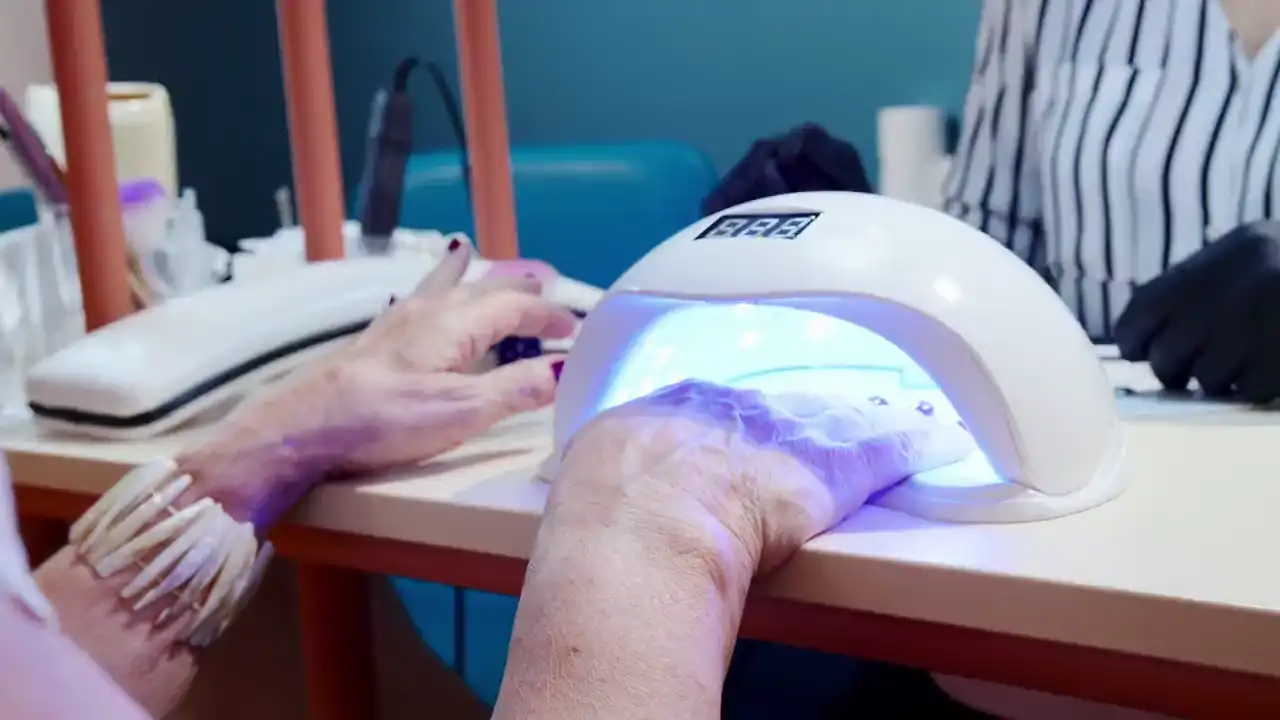 Eine Hand mit frisch lackierten Nägeln liegt unter einer LED-Lampe